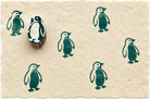 Hand carved penguin wooden block stamp displayed on handmade paper with repeating teal penguin prints.