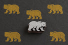 Hand-carved rustic bear wooden printing block displayed on dark handmade paper with repeated golden bear impressions.