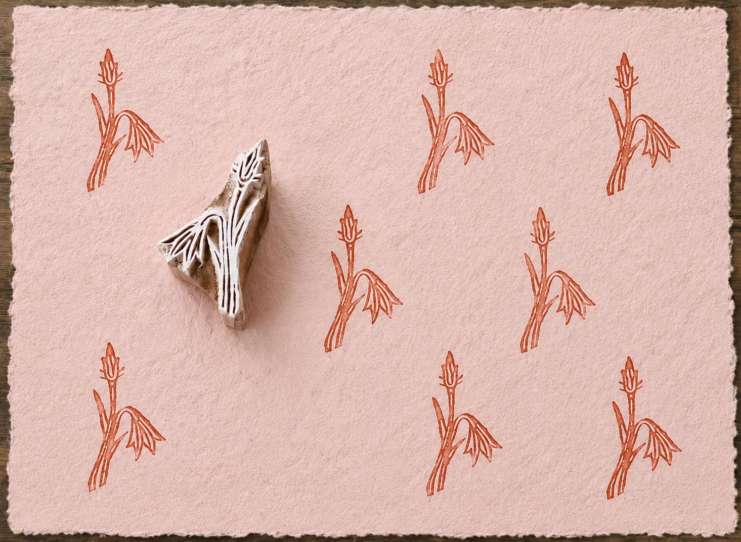 Hand carved snowdrop flower wooden block stamp displayed on pink handmade paper with repeating botanical impressions.