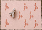 Hand carved snowdrop flower wooden block stamp displayed on pink handmade paper with repeating botanical impressions.
