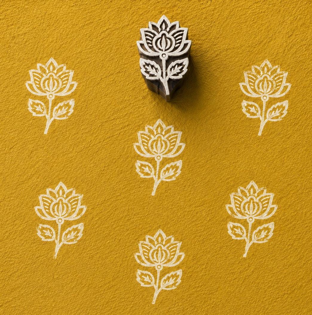 Hand carved folk lotus flower wooden printing block with repeated lotus impressions on textured mustard handmade paper.