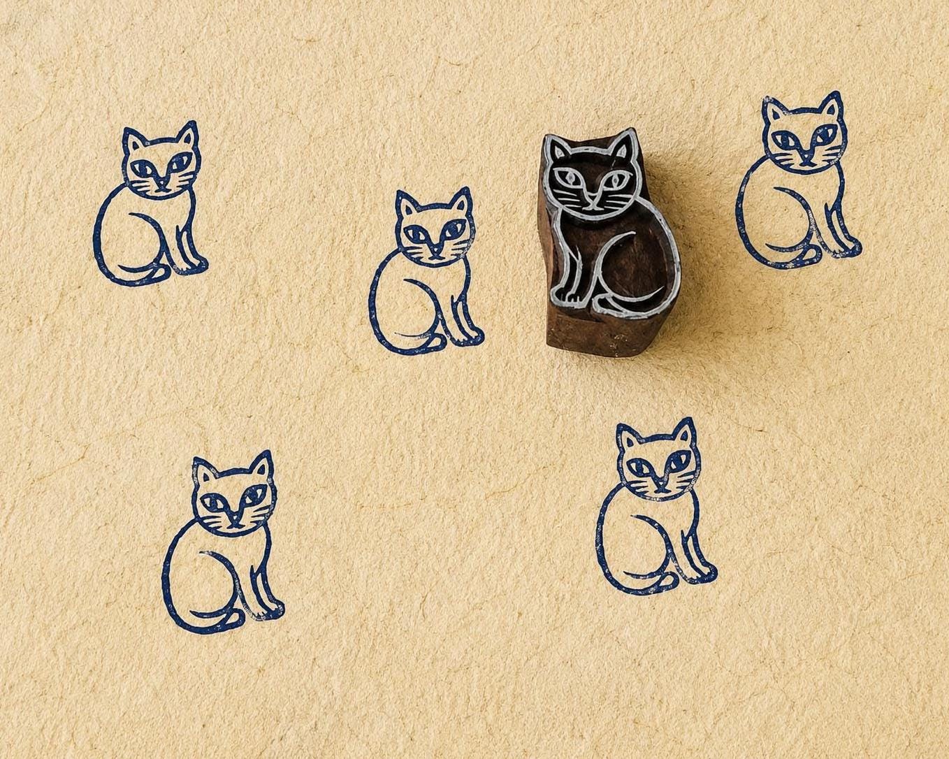 Hand-carved wooden sitting cat printing block with repeated indigo cat prints on handmade paper, traditional Indian block print stamp for fabric and paper crafts.