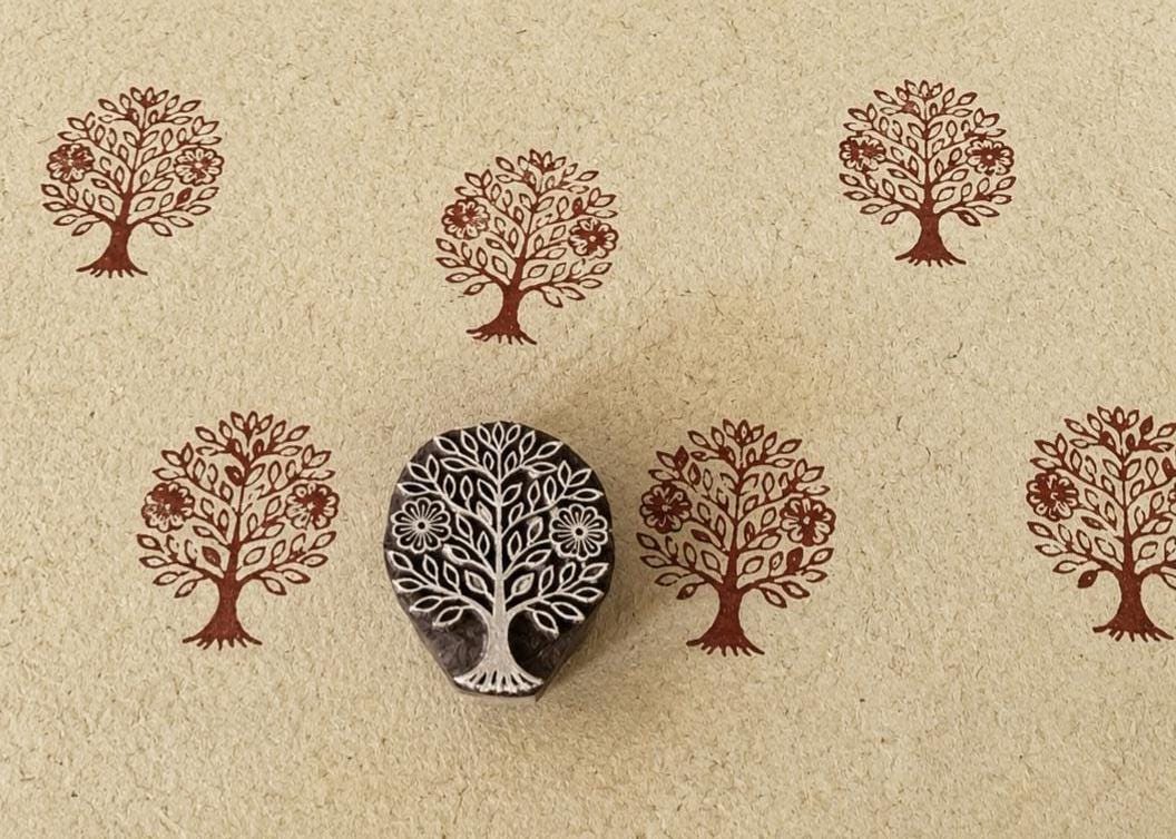 Hand-carved wooden floral tree printing block with repeated brown tree impressions on handmade paper, traditional Indian textile stamp for fabric and paper crafts.