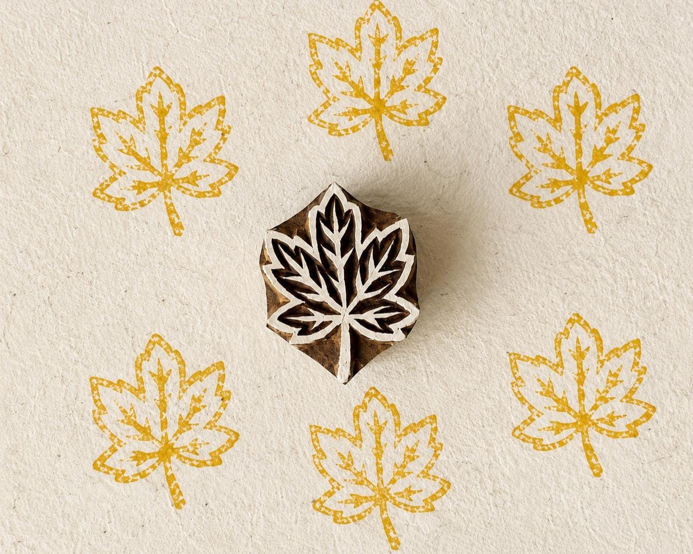 Hand-carved wooden Japanese maple leaf printing block with repeated golden yellow leaf impressions on handmade paper.