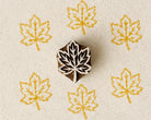 Hand-carved wooden Japanese maple leaf printing block with repeated golden yellow leaf impressions on handmade paper.