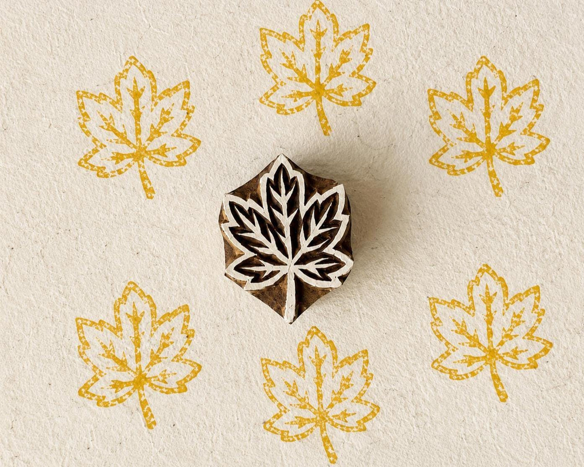 Hand-carved wooden Japanese maple leaf printing block with repeated golden yellow leaf impressions on handmade paper.