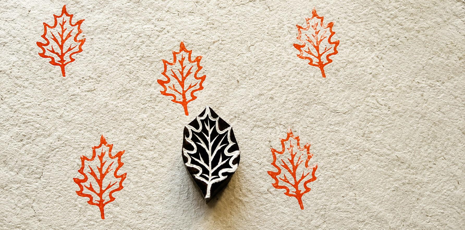Hand-carved wooden oak leaf printing block with repeated orange oak leaf impressions on handmade paper.