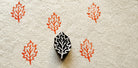Hand-carved wooden oak leaf printing block with repeated orange oak leaf impressions on handmade paper.