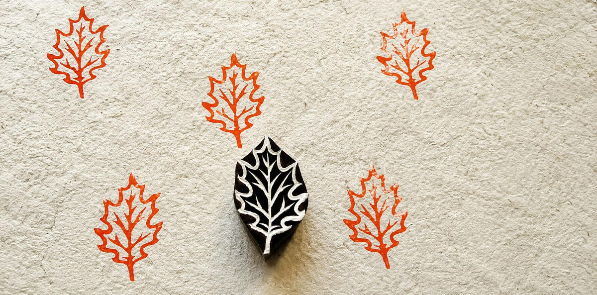 Hand-carved wooden oak leaf printing block with repeated orange oak leaf impressions on handmade paper.