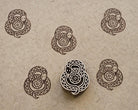 Hand-carved wooden folk art snake printing block with repeated brown coiled snake impressions on handmade paper.