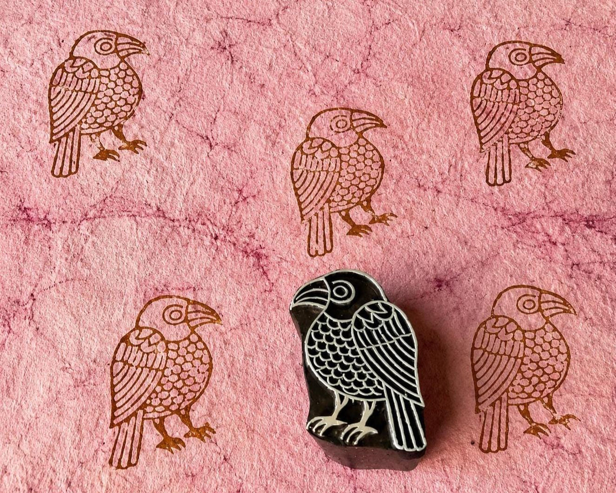 Hand-carved wooden storybook bird printing block with repeated brown bird impressions on pink handmade paper.