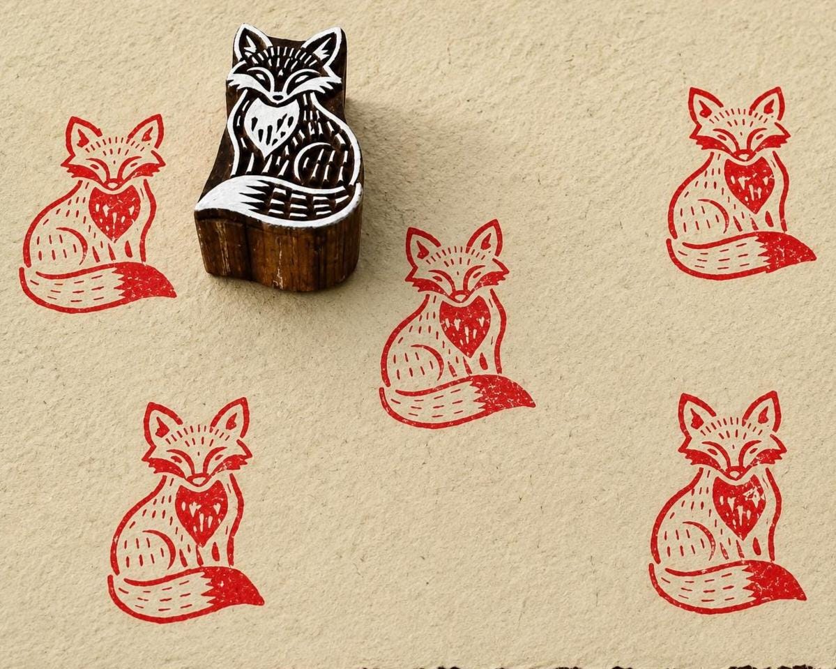 Hand-carved wooden curious fox printing block with repeated red fox impressions on handmade paper.
