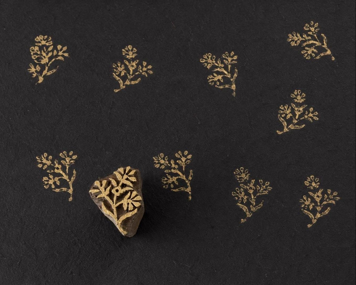 Hand carved wooden printing block featuring a delicate golden meadow sprig floral branch printed in metallic gold on black handmade paper.