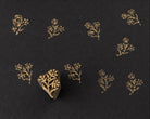 Hand carved wooden printing block featuring a delicate golden meadow sprig floral branch printed in metallic gold on black handmade paper.