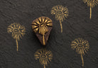 Hand carved wooden daisy bloom block printing stamp creating gold floral prints on handmade black paper.