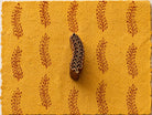 Hand carved wooden printing block featuring a paisley-inspired fern leaf design stamped repeatedly on mustard handmade paper using burgundy ink.