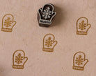 Hand-carved wooden snowflake mitten printing block with repeated mitten impressions on natural handmade paper, ideal for Christmas fabric printing, gift wrap, and holiday paper crafts.