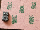 Hand-carved wooden folk art cat printing block with repeated green cat impressions on pink handmade paper.