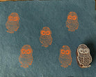 Hand-carved wooden cute owl printing block featuring an owl wearing a knitted hat, stamped in orange on teal handmade paper.