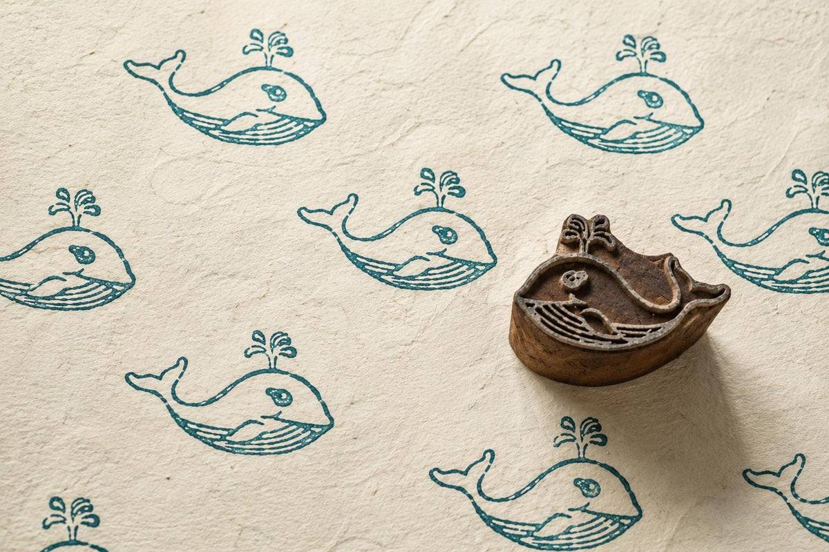 Hand-carved wooden whale printing block with cute whale impressions on handmade paper, ideal for fabric printing, journaling, pottery, wrapping paper, and DIY crafts.
