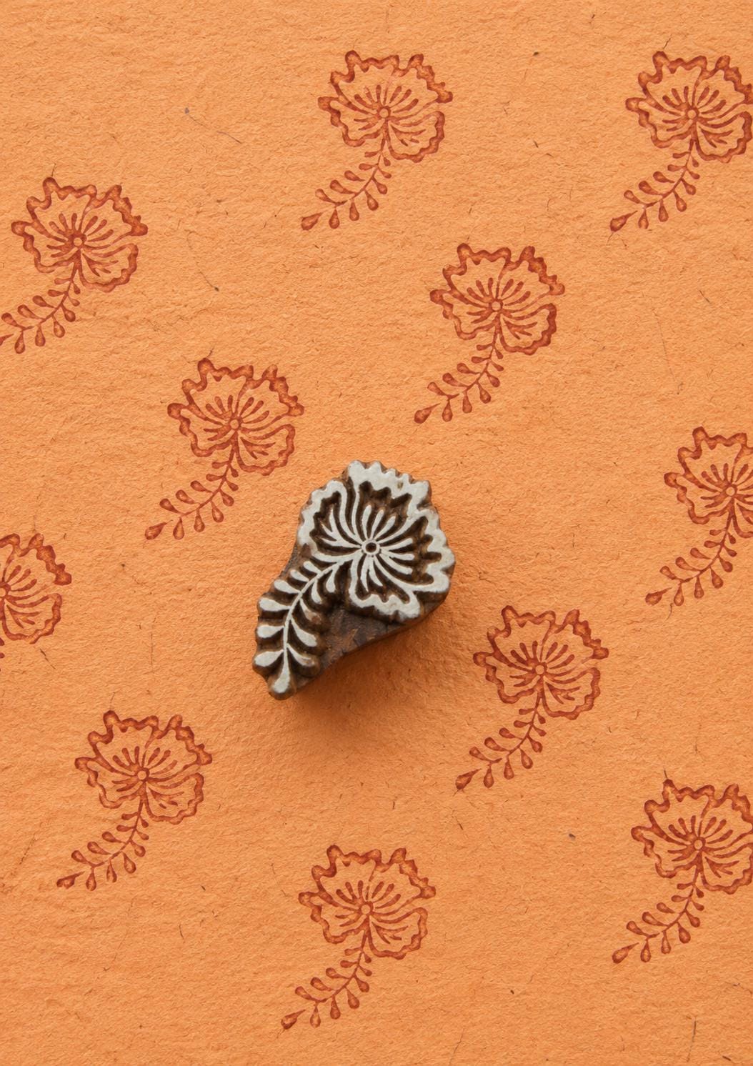 Hand-carved wooden poppy flower printing block with terracotta floral impressions on orange handmade paper for fabric printing, pottery, journals, and paper crafts.