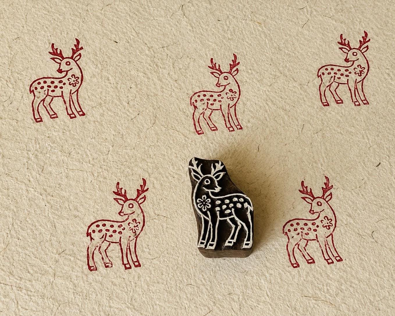 Hand-carved wooden floral deer printing block with repeated burgundy deer impressions on handmade paper.