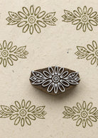 Hand-carved daisy flower wooden printing block surrounded by repeated olive green floral impressions on textured natural handmade paper.