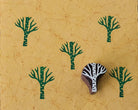 Hand-carved wooden winter tree printing block with repeated green branch impressions on handmade paper.