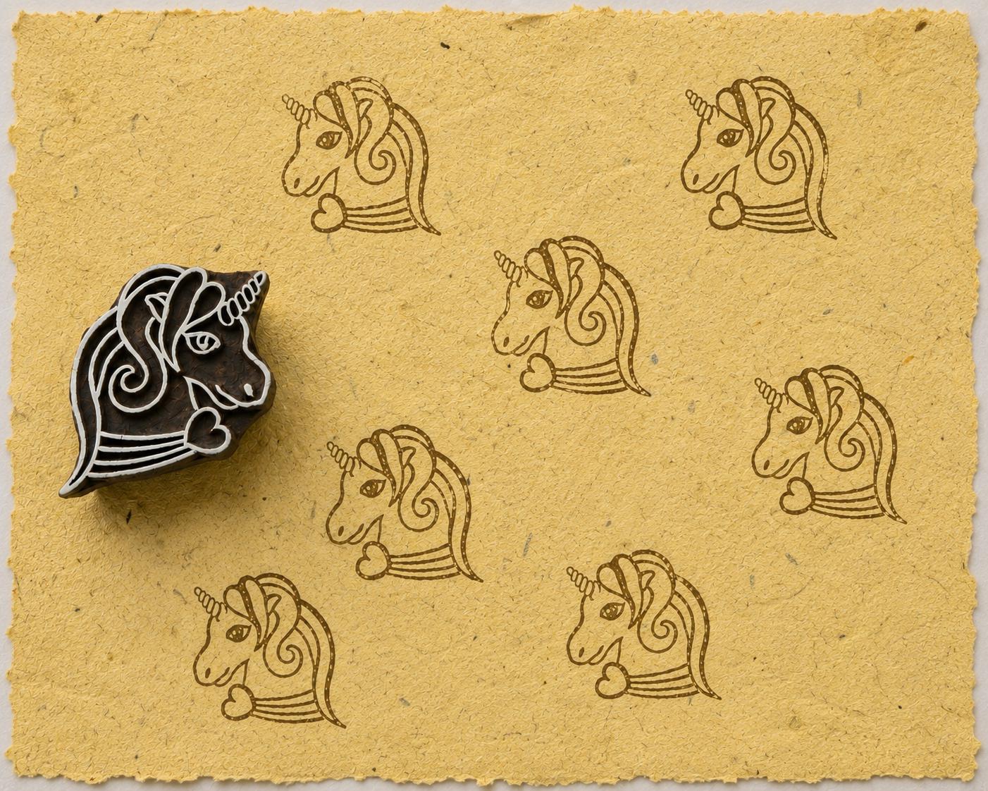 Hand-carved unicorn wooden printing block with repeated brown unicorn impressions on textured mustard yellow handmade paper.