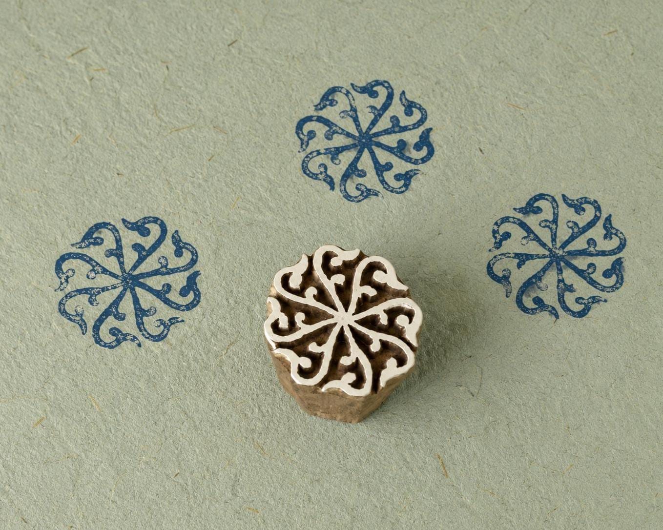 Hand carved wooden printing block featuring a circular scroll rosette motif with blue stamped impressions on handmade paper.