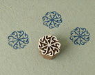 Hand carved wooden printing block featuring a circular scroll rosette motif with blue stamped impressions on handmade paper.
