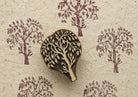 Hand carved wooden printing block featuring a twisted willow tree design stamped repeatedly on handmade textured paper in muted plum ink