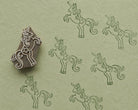 Hand carved wooden printing block featuring a prancing unicorn design with repeated dark green impressions on textured sage handmade paper.
