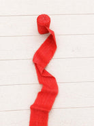 Single roll of extra wide vermilion sari silk ribbon unrolling to showcase its rich texture and frayed edges.