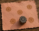 Hand-carved Sunburst Bloom wooden printing block with floral impressions on blush handmade paper.