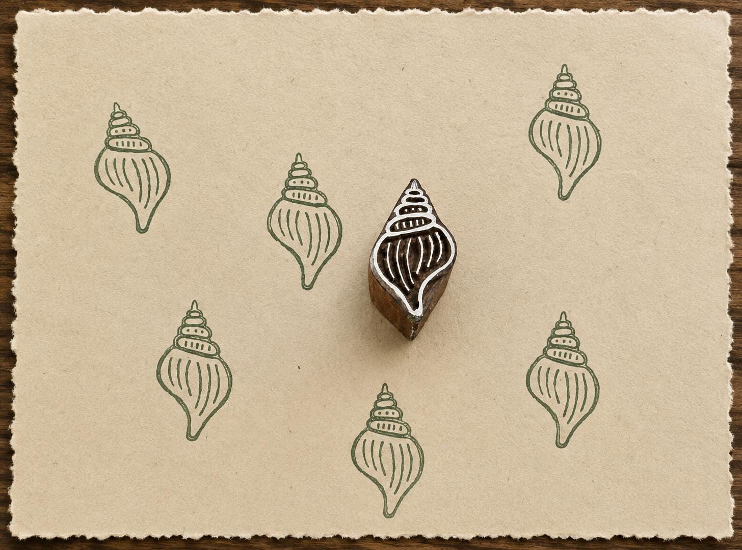 Hand-carved Whelk Shell wooden printing block with sage green shell impressions on textured handmade cream paper.