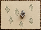 Hand-carved Whelk Shell wooden printing block with sage green shell impressions on textured handmade cream paper.