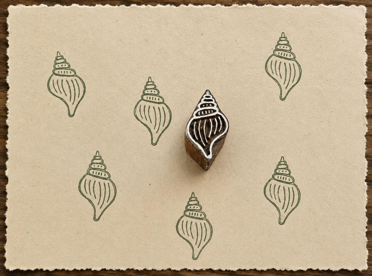 Hand-carved Whelk Shell wooden printing block with sage green shell impressions on textured handmade cream paper.