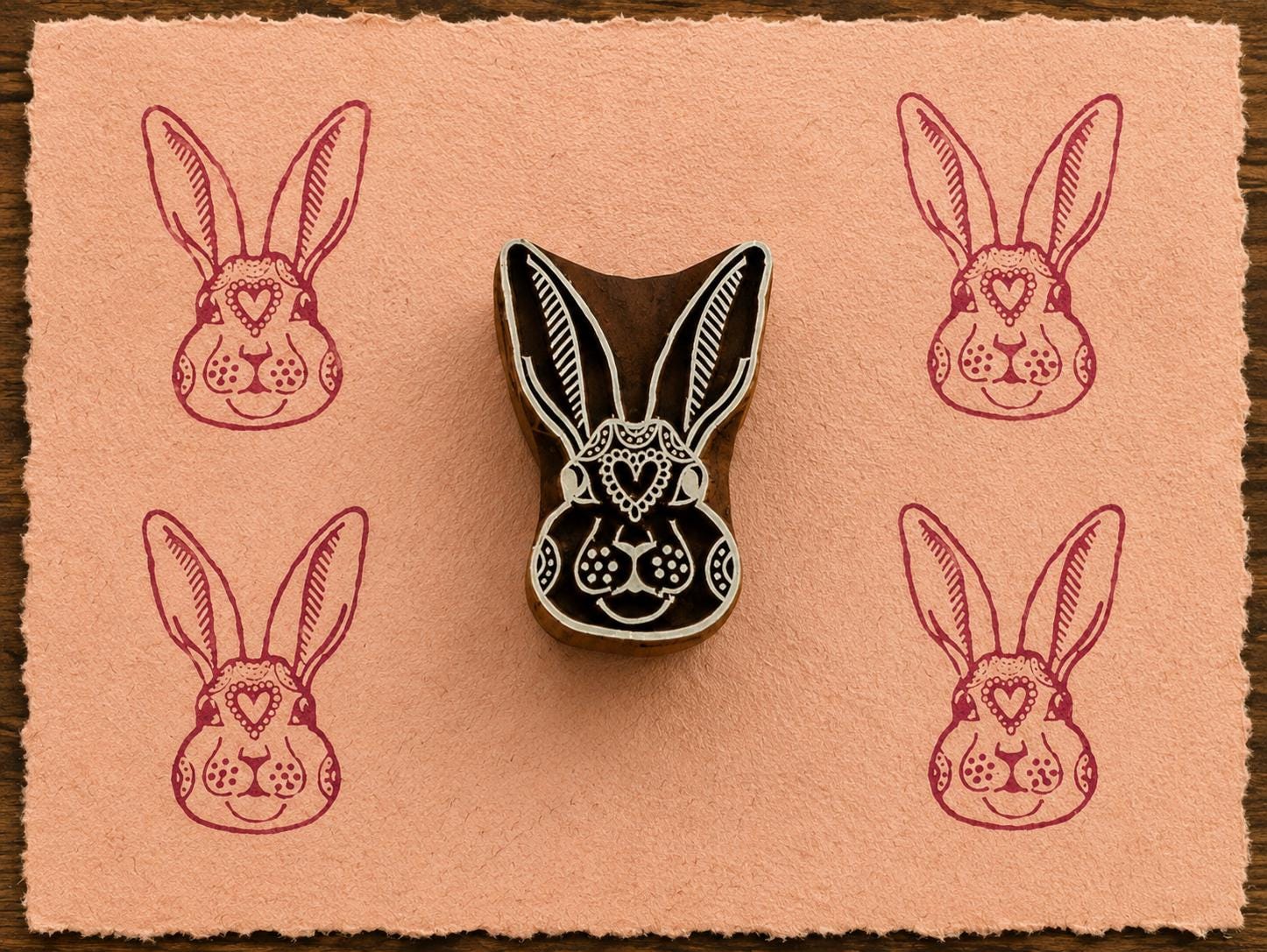 Hand-carved Heart Bunny wooden printing block with magenta rabbit impressions on blush handmade paper.