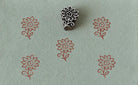 Hand-carved wooden floral printing block with repeated rustic blossom impressions on sage green handmade paper, ideal for fabric printing, stationery, and DIY crafts.