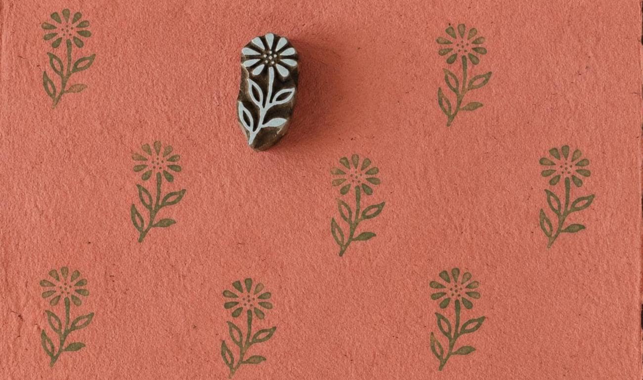 Hand-carved wooden floral printing block with repeated wild meadow flower impressions on coral handmade paper, perfect for fabric printing, stationery, and botanical crafts.