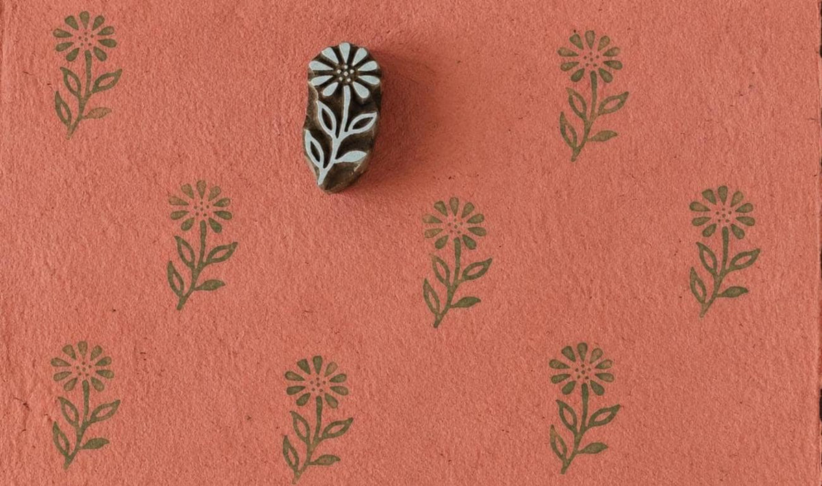 Hand-carved wooden floral printing block with repeated wild meadow flower impressions on coral handmade paper, perfect for fabric printing, stationery, and botanical crafts.