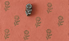 Hand-carved wooden floral printing block with repeated wild meadow flower impressions on coral handmade paper, perfect for fabric printing, stationery, and botanical crafts.