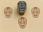 Hand-carved Sugar Skull wood block stamp with detailed brown calavera impressions on handmade cream paper.