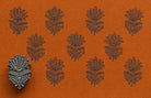 Hand-carved Indian floral wooden printing block displayed beside repeated dark blue botanical impressions on textured orange handmade paper.