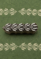 Hand-carved floral vine border wooden printing block with repeated cream leafy border impressions on textured dark green handmade paper.