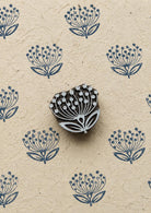 Hand-carved dandelion flower wooden printing block surrounded by repeated navy blue botanical impressions on textured handmade paper.