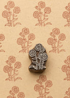 Hand-carved wooden block with three daisy flowers and leafy stems, surrounded by repeated terracotta floral prints on textured handmade paper.