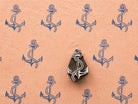 Hand-carved wooden anchor printing block with rope detail surrounded by repeated blue anchor prints on textured peach handmade paper.