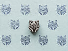 Hand-carved tribal cat wooden printing block displayed on pale blue handmade paper with repeating blue geometric cat face impressions.
